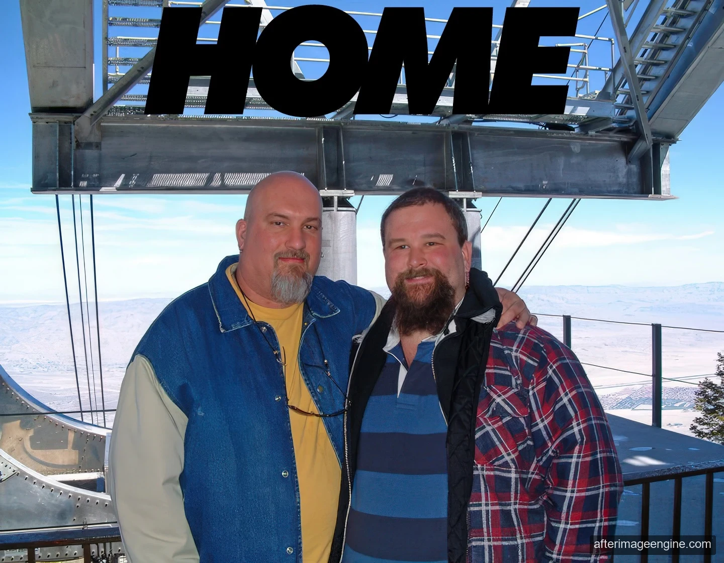 Two men pose in bright daylight beneath large black HOME lettering, with a canyon beyond.